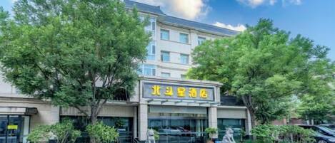 A hotel with a signboard, surrounded by trees and a parking area.