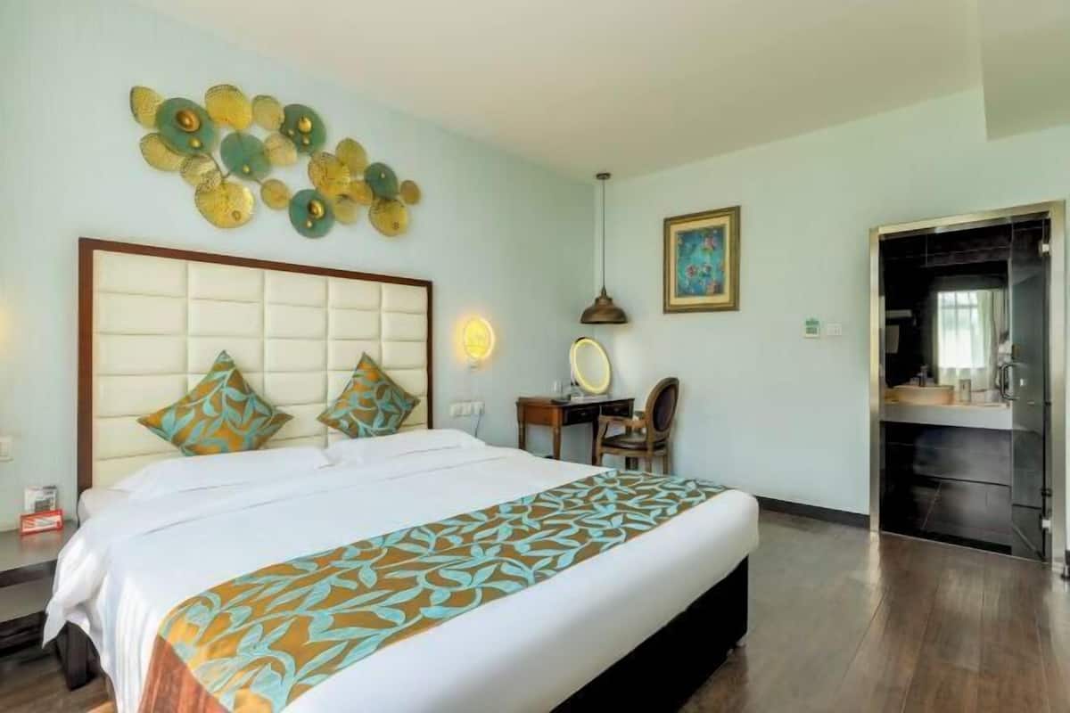 A hotel room with a bed, a desk, a chair, a mirror, and a kitchenette.