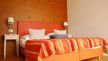 Ein Hotelzimmer mit Holz-Kopfteil, einem Bett mit weißer und orangefarbener Bettwäsche, zwei Nachttischen mit Lampen und einem Holzboden.