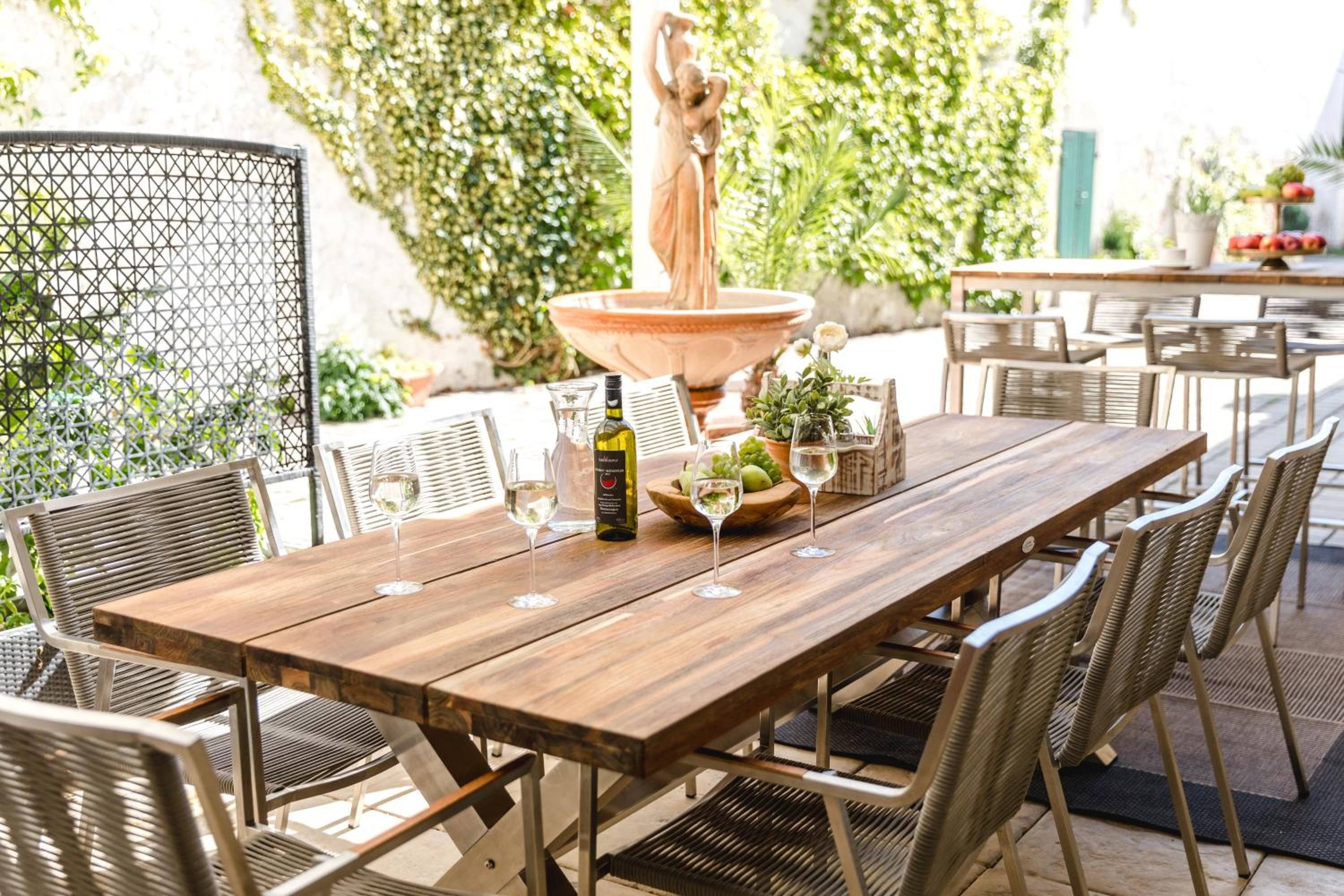 An outdoor dining area with a wooden table and wicker chairs, a statue, and a fountain.