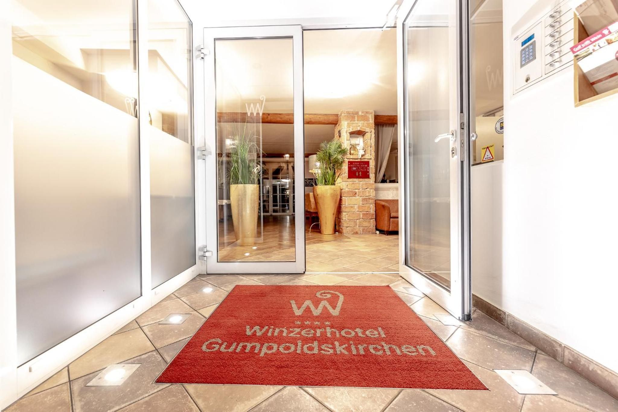 A hotel entrance with a red carpet, glass doors, and a visible reception area.
