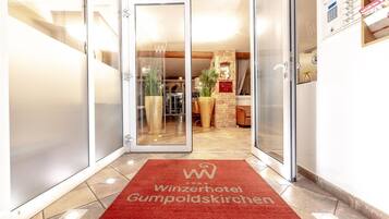 A hotel entrance with a red carpet, glass doors, and a visible reception area.