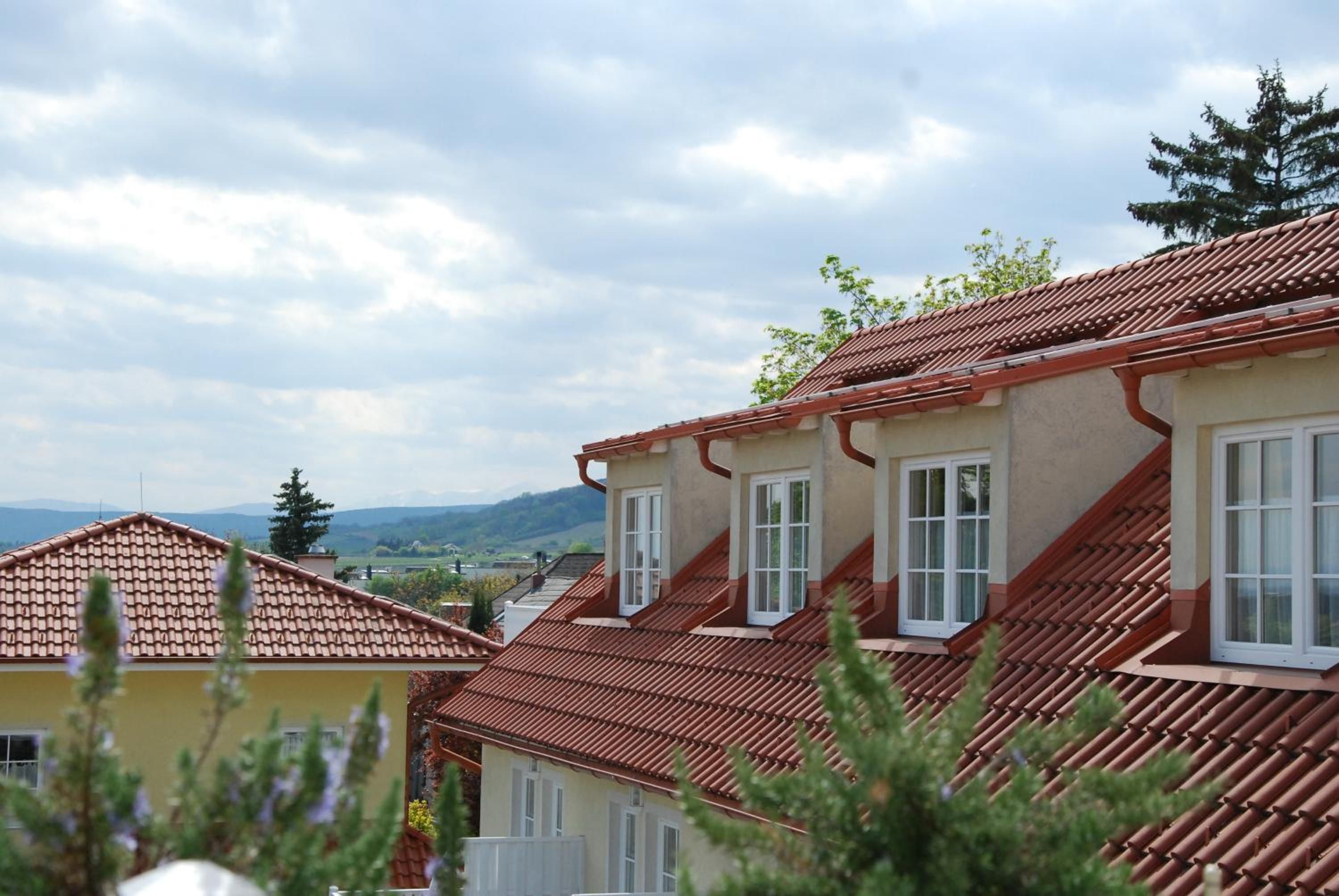 Ein Wohngebäude mit rotem Ziegeldach, zahlreichen Fenstern und Blick auf eine hügelige Landschaft.