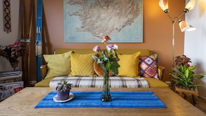 Un salón acogedor con una mesa de centro de madera, un jarrón con flores, un mapa en la pared y un sofá con cojines amarillos.
