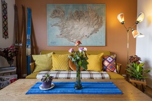 Un salón acogedor con una mesa de centro de madera, un jarrón con flores, un mapa en la pared y un sofá con cojines amarillos.