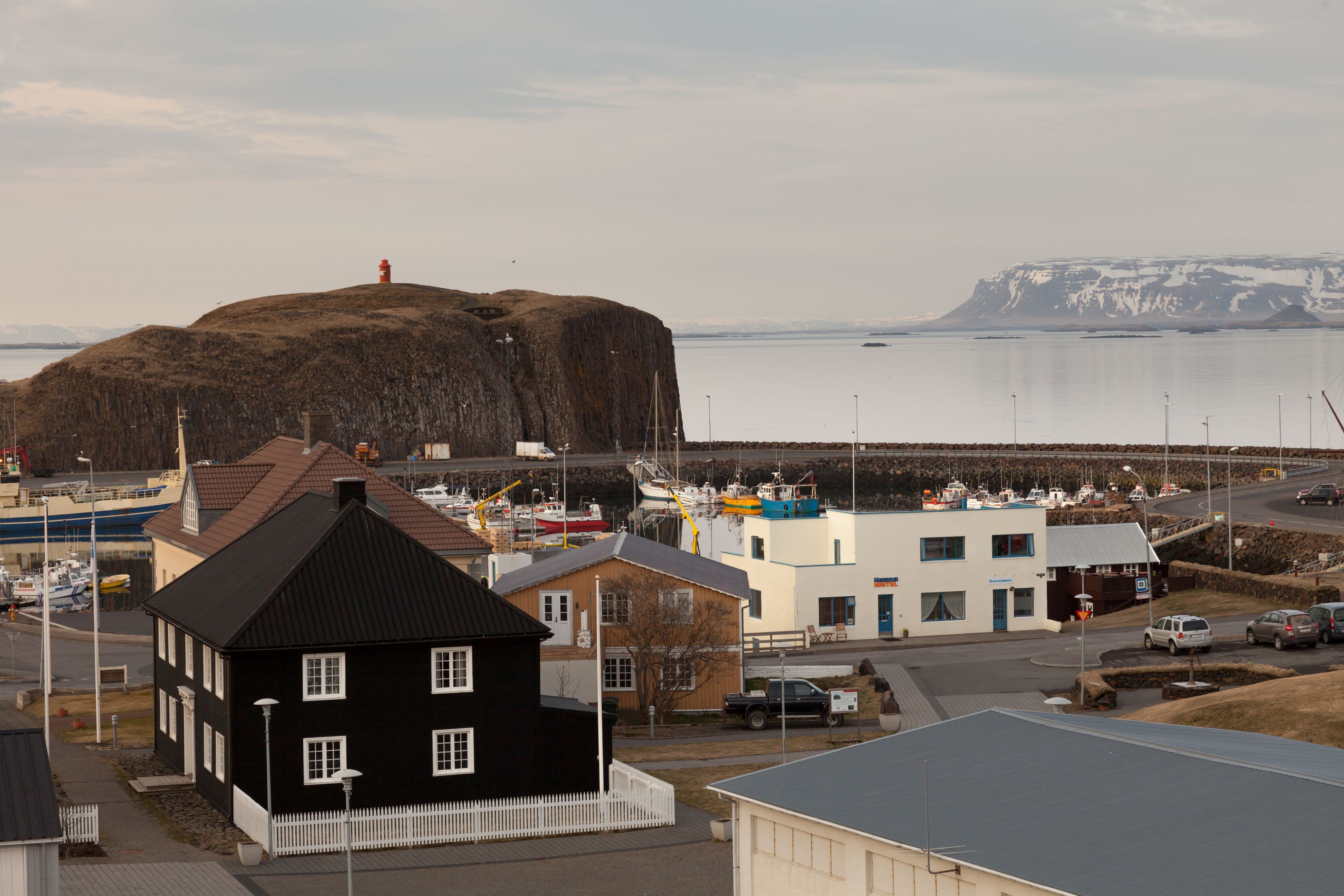 A coastal town with a prominent rock formation, a lighthouse, and a marina with boats.