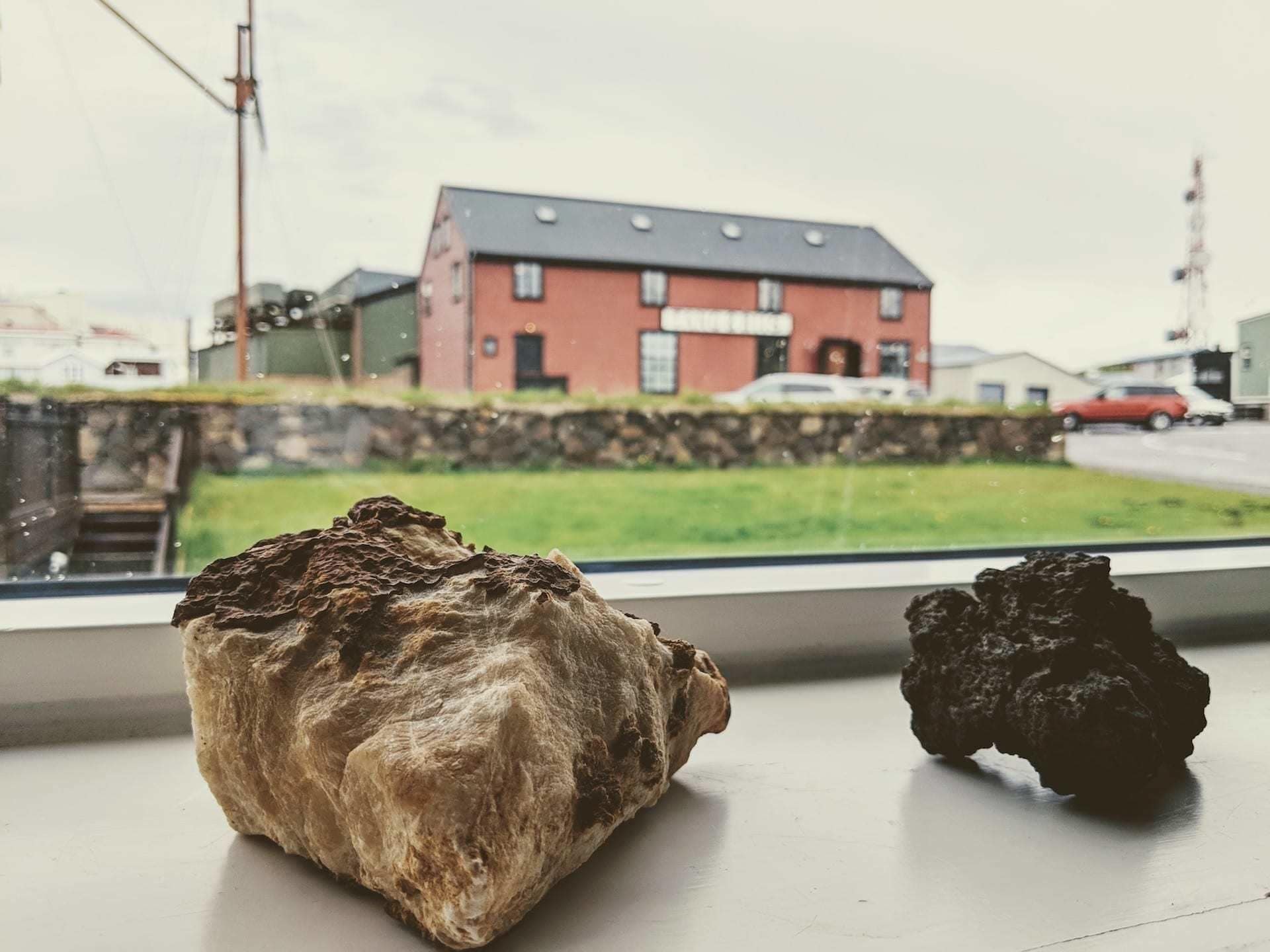 Two rocks on a windowsill with a view of a red building and a stone wall in the background.