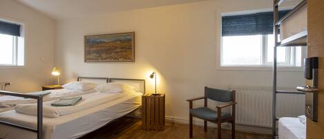 A hotel room with two beds, a chair, a painting, and a radiator.