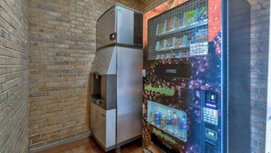 A vending machine with a digital display and a push button, next to a stainless steel refrigerator in a room with brick walls. - Motel 6 Falls Church, VA - Arlington Boulevard (Falls Church)