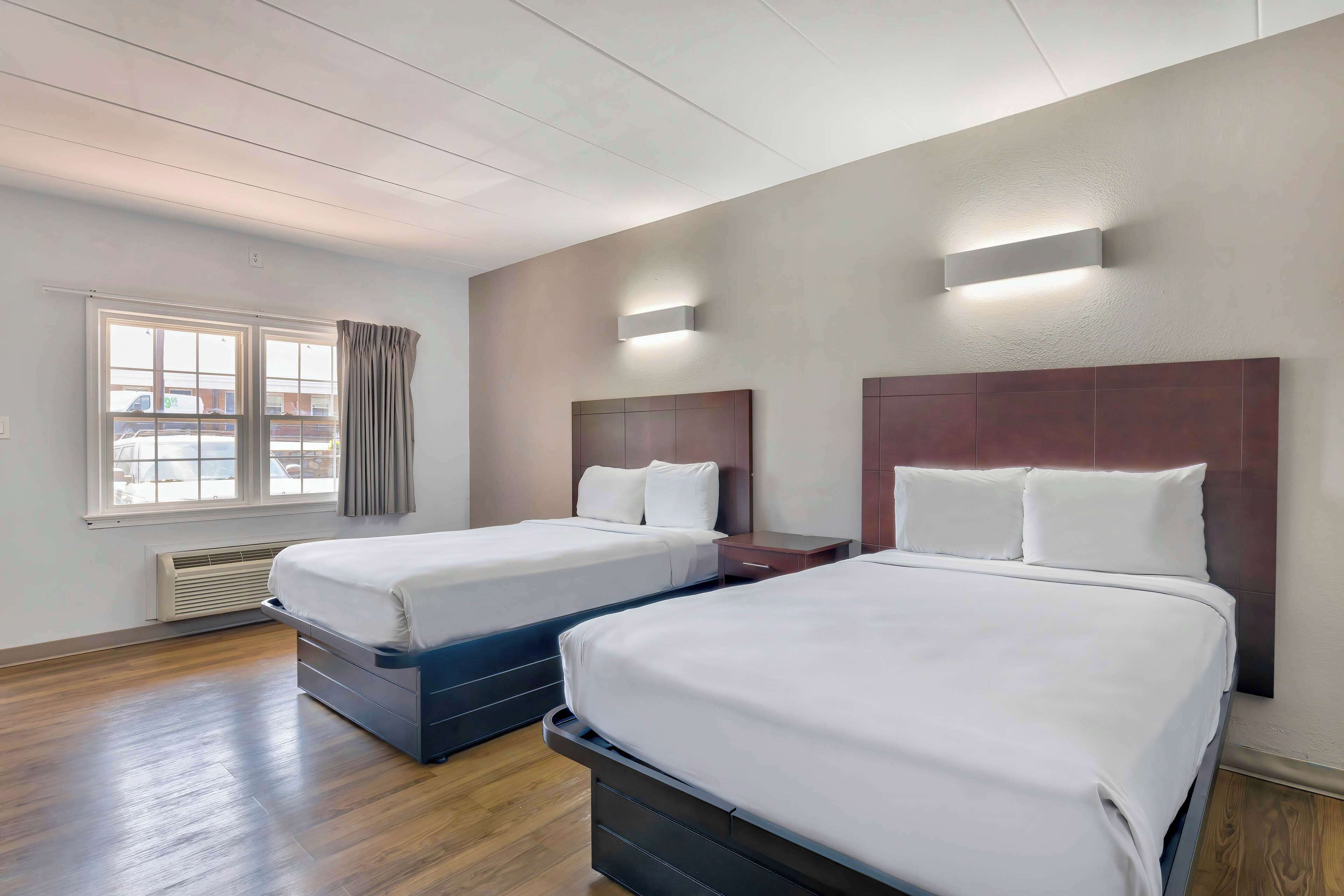 Habitación de hotel con dos camas, una ventana con cortinas, una lámpara de pared y un radiador.