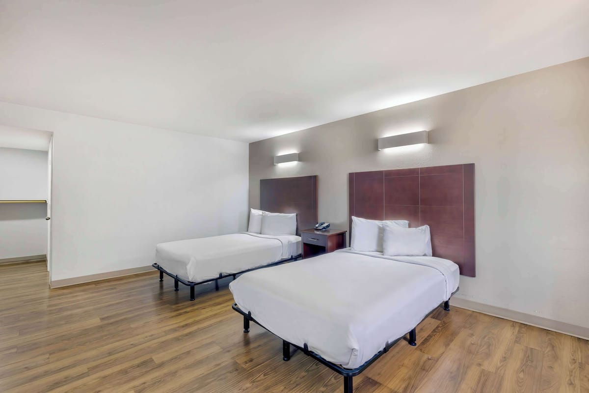 A hotel room with two beds, a wooden floor, and a small desk with a telephone.