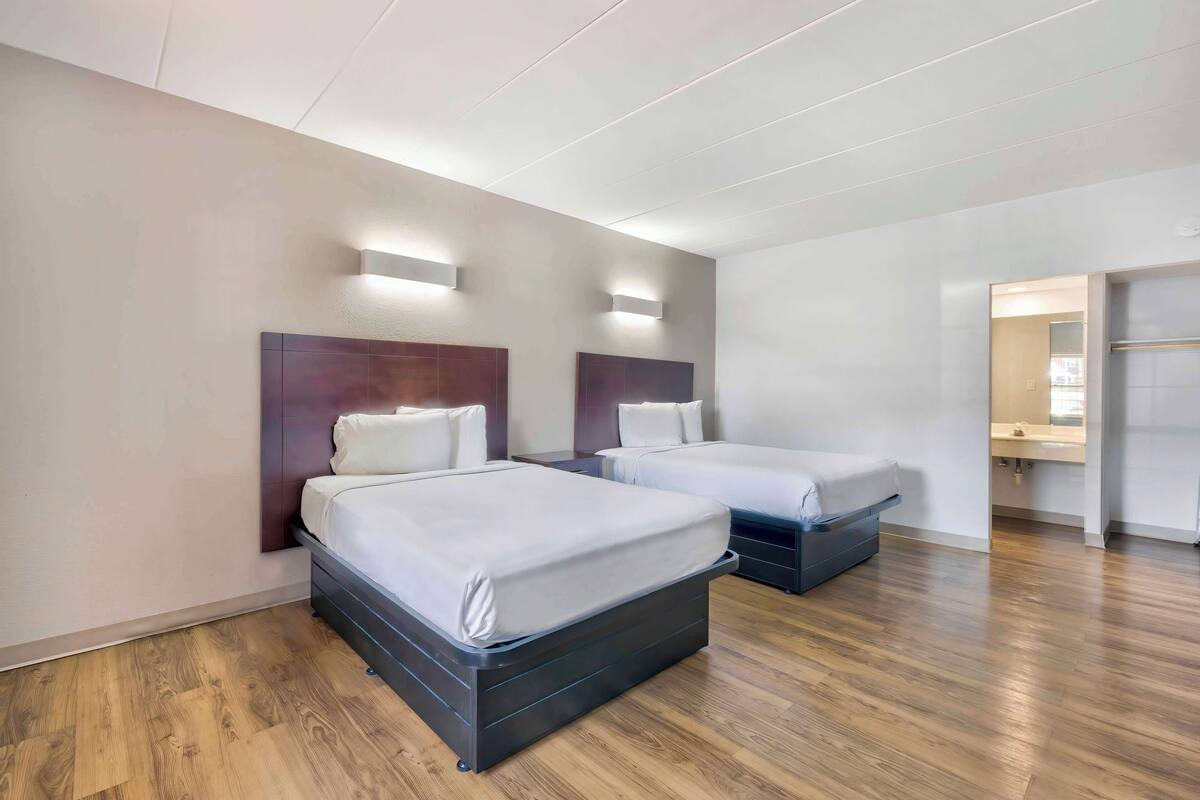 A modern hotel room with two beds, wooden flooring, and built-in headboards.