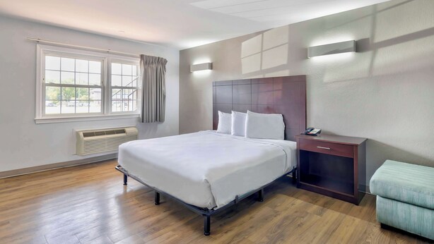 A hotel room with a large bed, a bedside table with a phone, a heater, and a window with curtains. - Motel 6 Falls Church, VA - Arlington Boulevard (Falls Church)