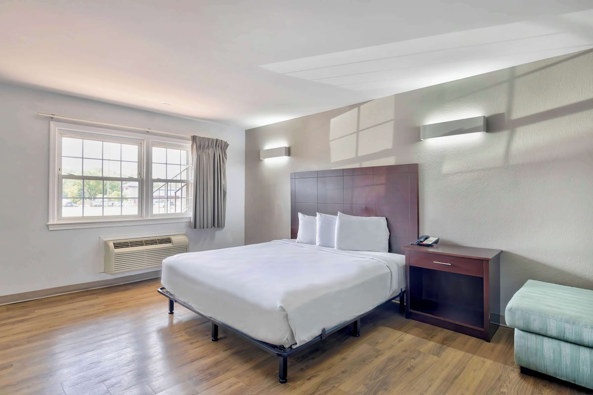 A hotel room with a large bed, a bedside table with a phone, a heater, and a window with curtains.