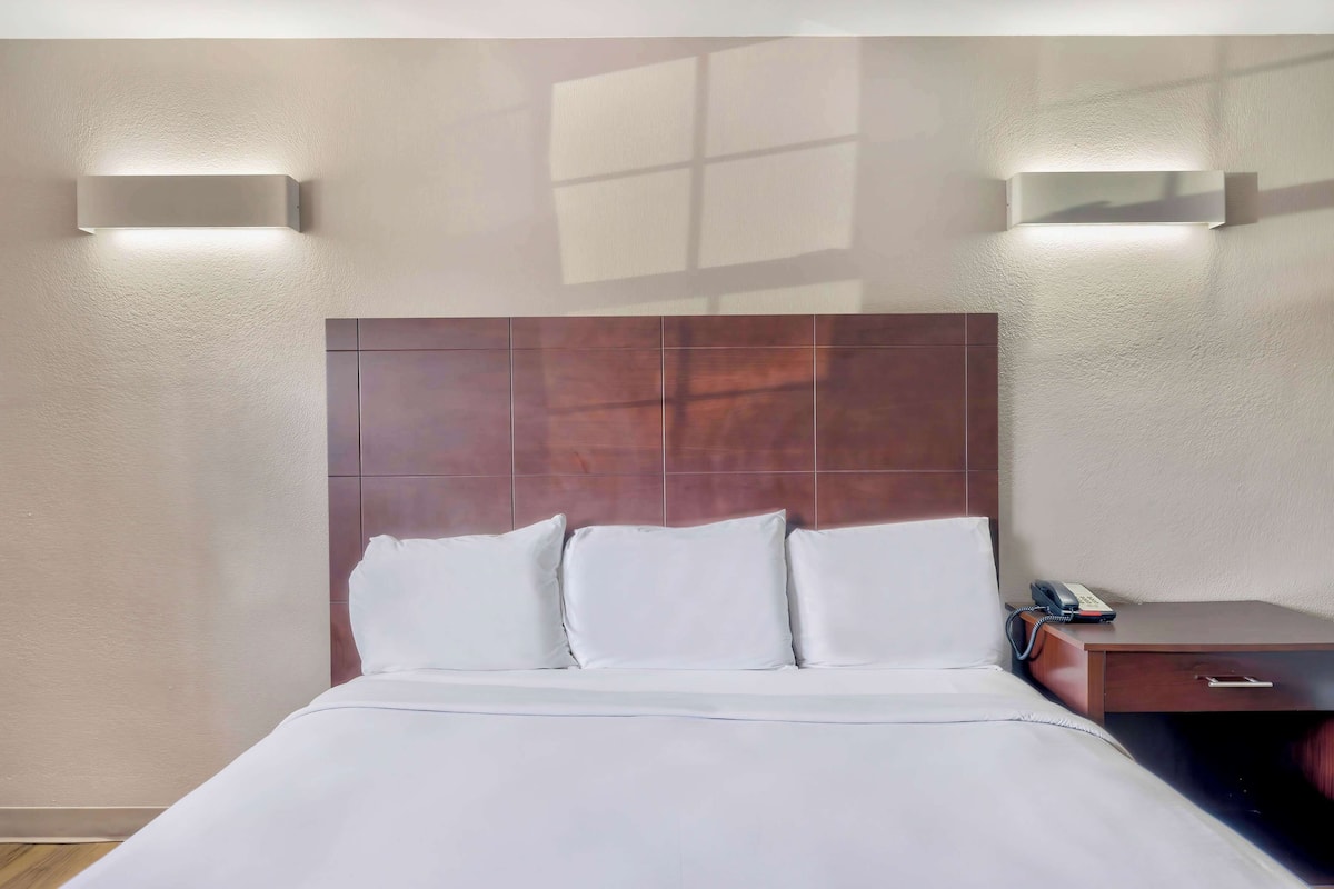 A hotel room with a large bed, a wooden headboard, and two wall-mounted lights.