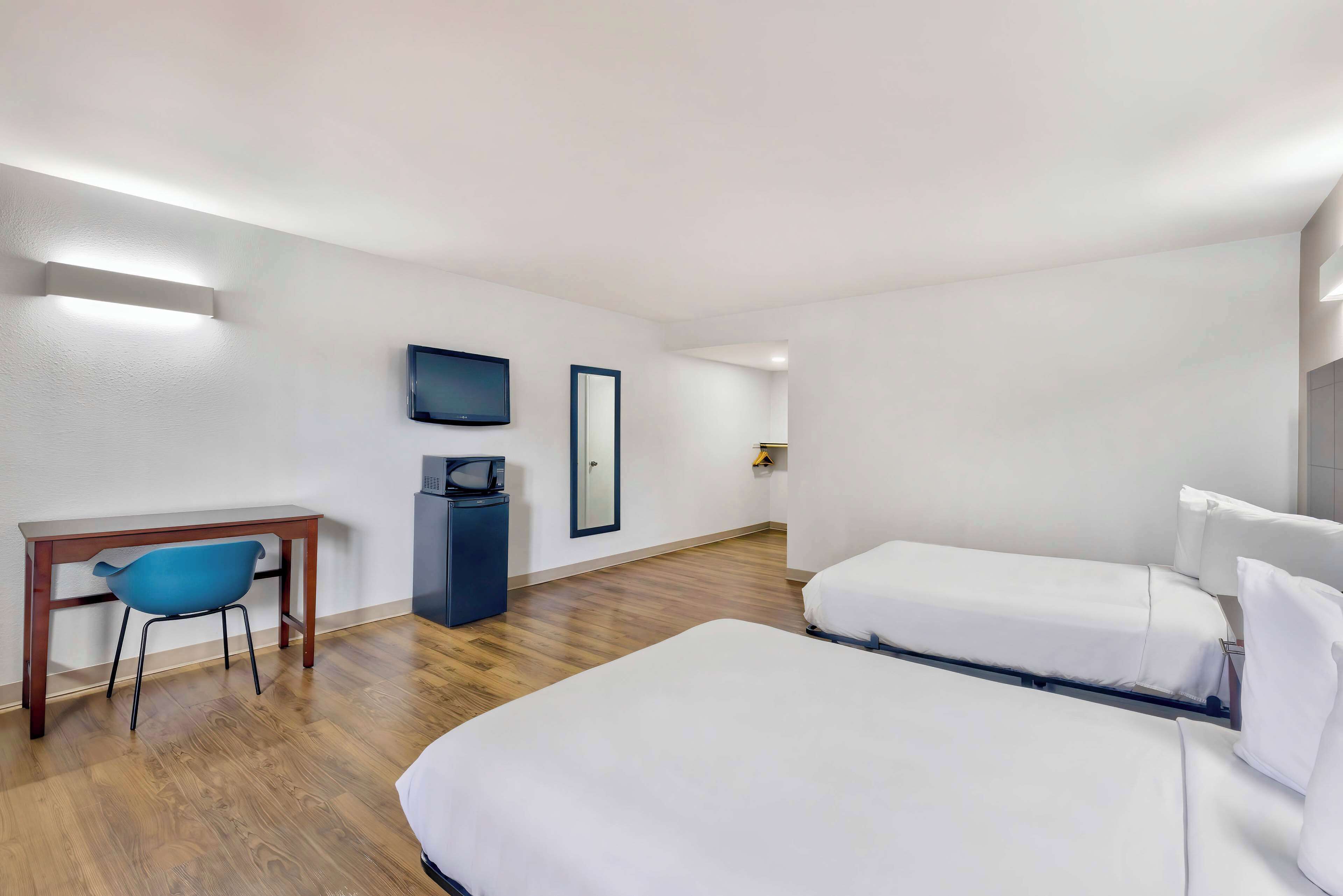 Une chambre d’hôtel avec un plancher en bois, un bureau avec une chaise, deux lits, une télévision et un miroir.