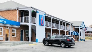 A motel with a 'Welcome' sign, a car parked in front, and a '6' sign indicating the number of rooms. - Motel 6 Falls Church, VA - Arlington Boulevard (Falls Church)