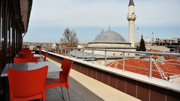 Una terraza en la azotea con sillas y mesas rojas, con vista a una mezquita con cúpula y alminar.