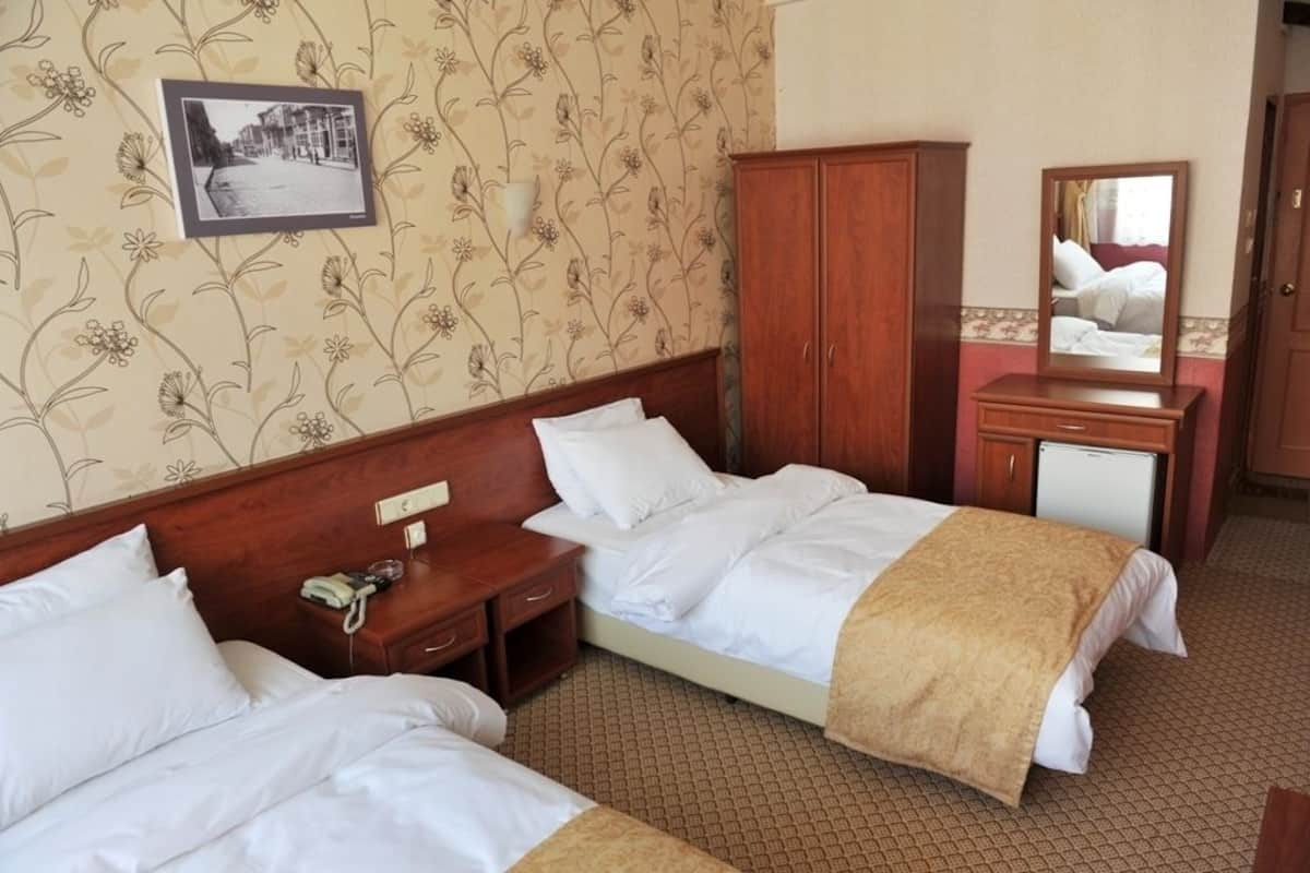 Quarto de hotel com duas camas, um guarda-roupa de madeira, uma mesa de cabeceira com telefone e um espelho.