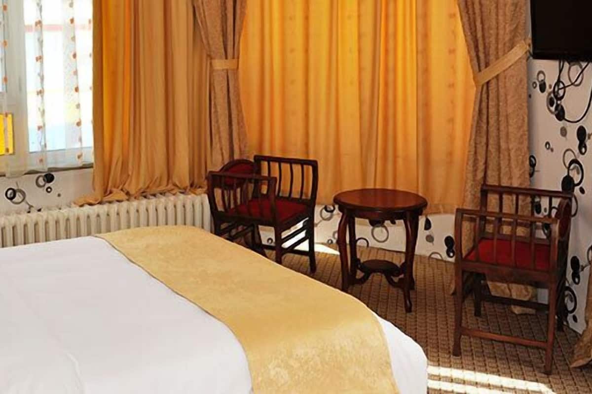 Quarto de hotel com cama, duas cadeiras, uma mesinha e um radiador.