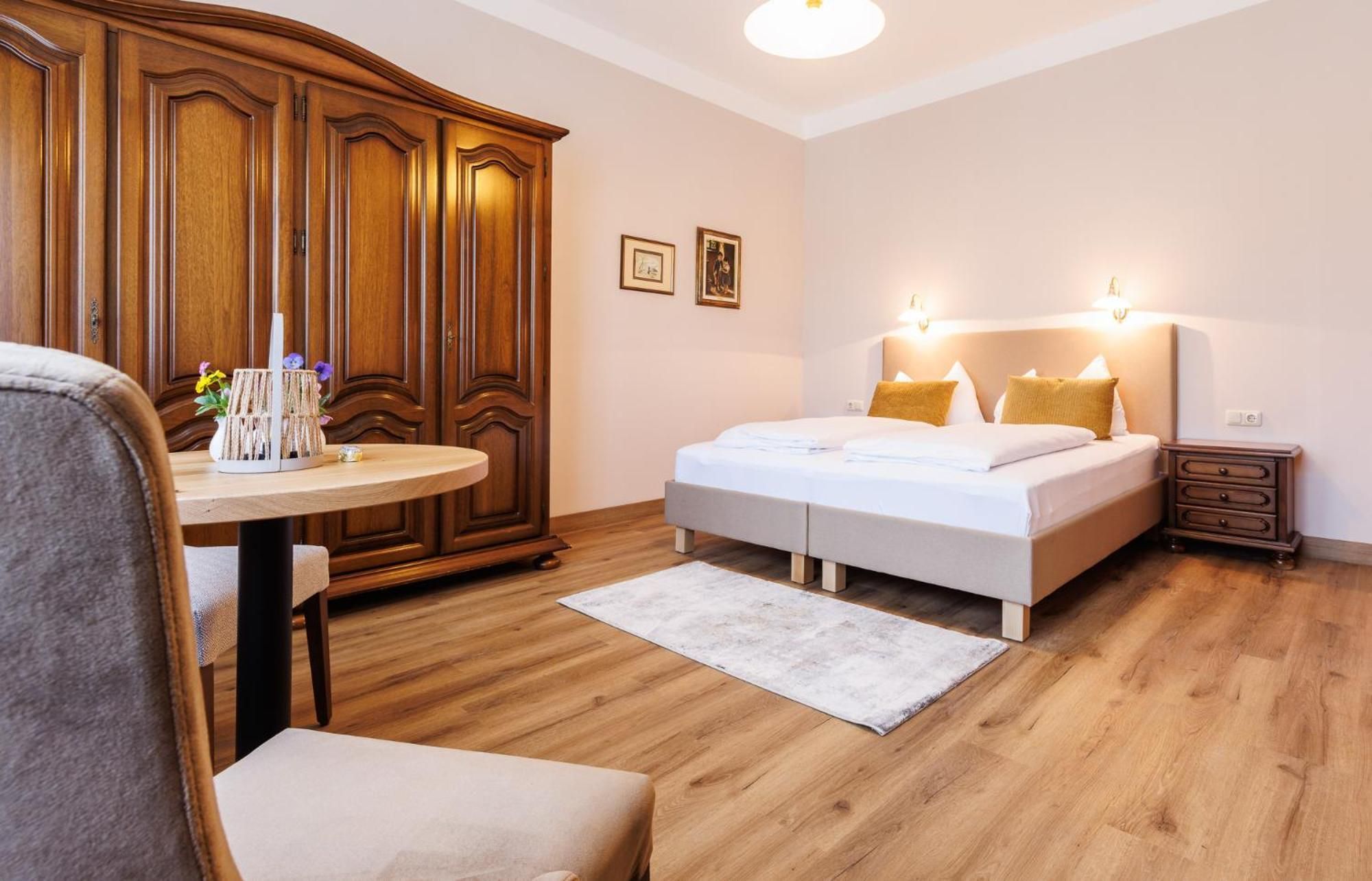 Une chambre à coucher comprenant un lit, des tables de chevet, une armoire, une table ronde avec un vase et une chaise.