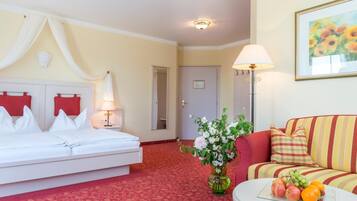 Une chambre d’hôtel avec un lit, un canapé, une lampe, un vase de fleurs et un panier de fruits.