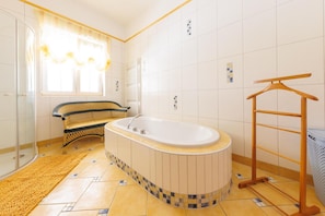 A bathroom with a bathtub, a wicker bench, a wooden drying rack, and a patterned floor.