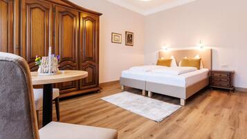 Un dormitorio con cama, mesitas de noche, armario, una mesa redonda con un florero y una silla.