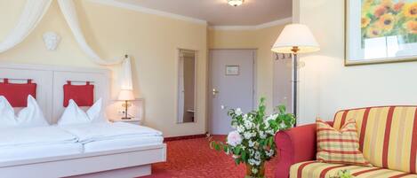 A hotel room with a bed, a sofa, a lamp, a vase with flowers, and a fruit bowl.