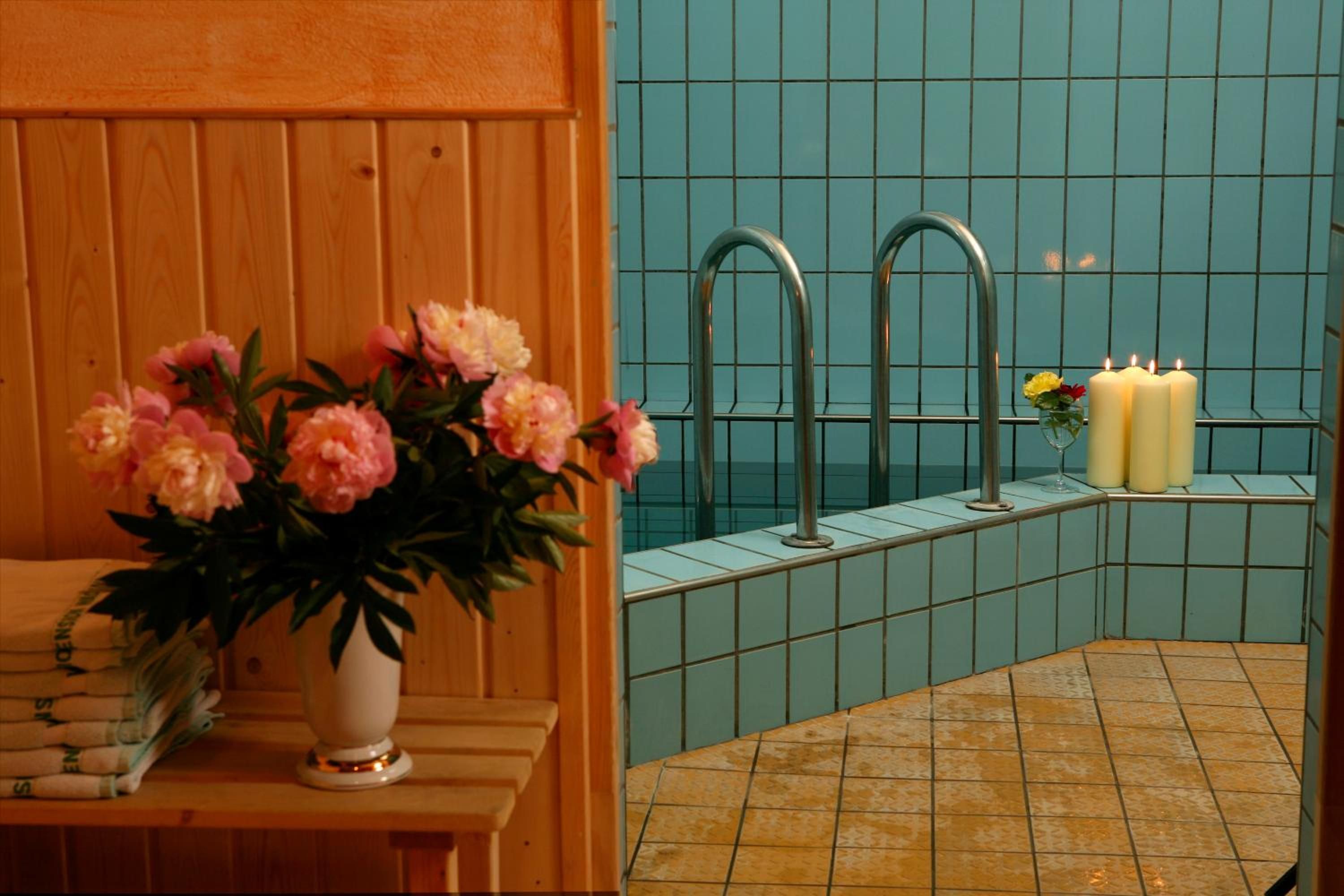 A bathroom with a wooden vanity, a vase of flowers, and a tiled wall with a faucet and candles.