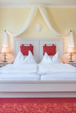 A double bed with white linens, two red pillows, and a canopy overhead.
