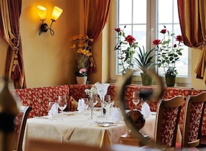 A dining area with a table set for two, a window with curtains, and a wall-mounted light fixture.