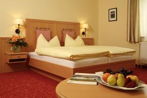 A hotel room with a bed, bedside tables, a lamp, a vase of flowers, a fruit plate, and a framed picture on the wall.