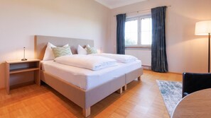 A hotel room with a bed, bedside tables, a lamp, a chair, and a window with curtains.