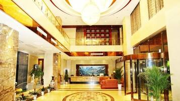 A hotel lobby with a reception desk, seating area, and a large chandelier.