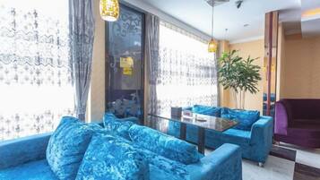 A modern hotel lobby with blue sofas, a glass coffee table, and a large plant.