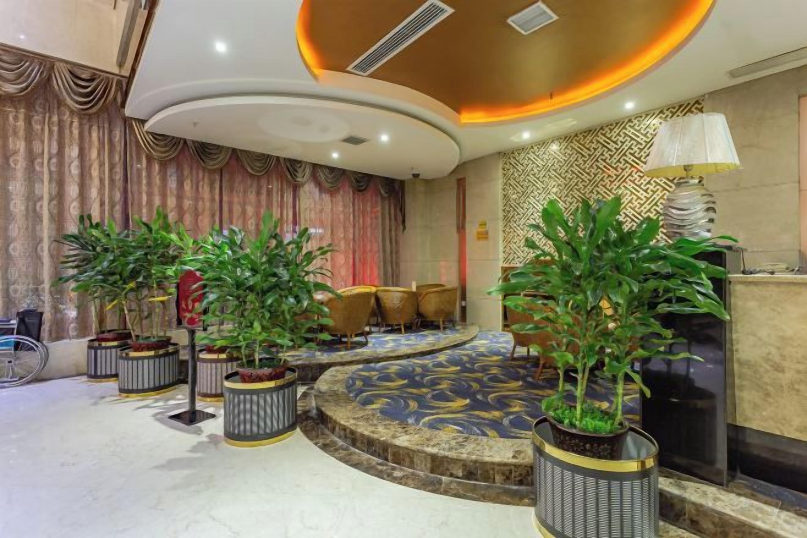 A lobby with a circular seating area, potted plants, and a patterned carpet.