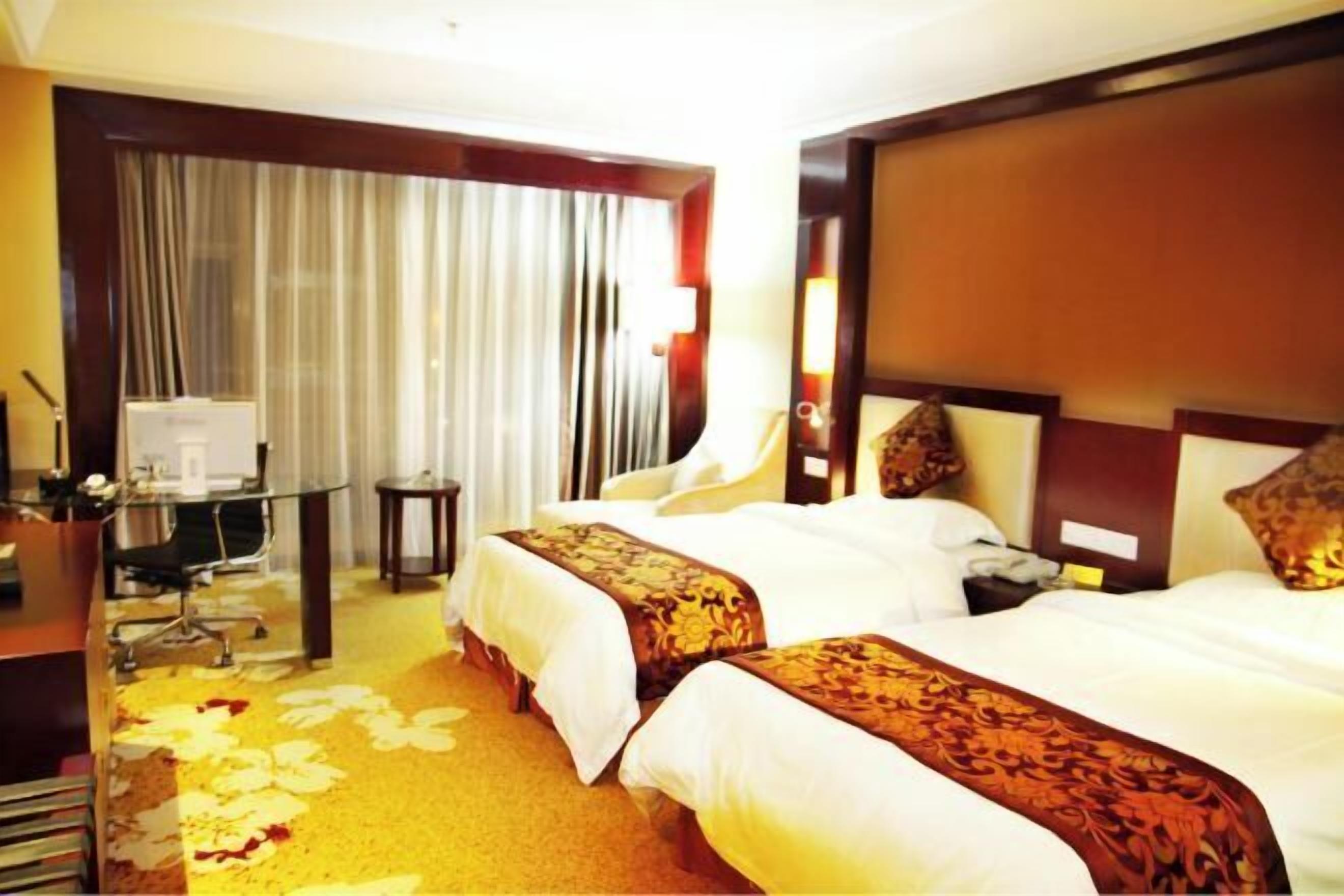 Une chambre d’hôtel avec deux lits, un bureau, une chaise, une petite table et une fenêtre avec des rideaux.
