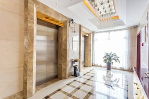 Un vestíbulo de hotel con piso de mármol, un ascensor, una recepción y un ventanal grande.