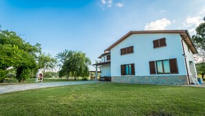 A two-story house with a stone base and a light blue upper section, featuring a patio with outdoor furniture. - Villa Leonardo (Sarteano)