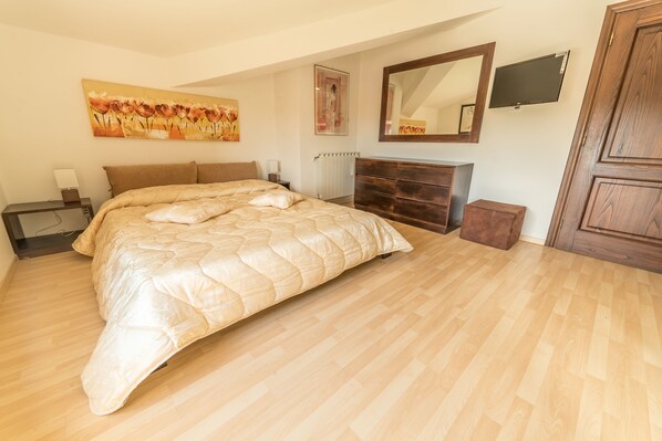 Une chambre à coucher avec un grand lit, une commode, un miroir et un téléviseur fixé au mur.
