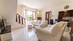 A modern living room with a sofa, ottoman, and a TV on a stand. - Villa Leonardo (Sarteano)