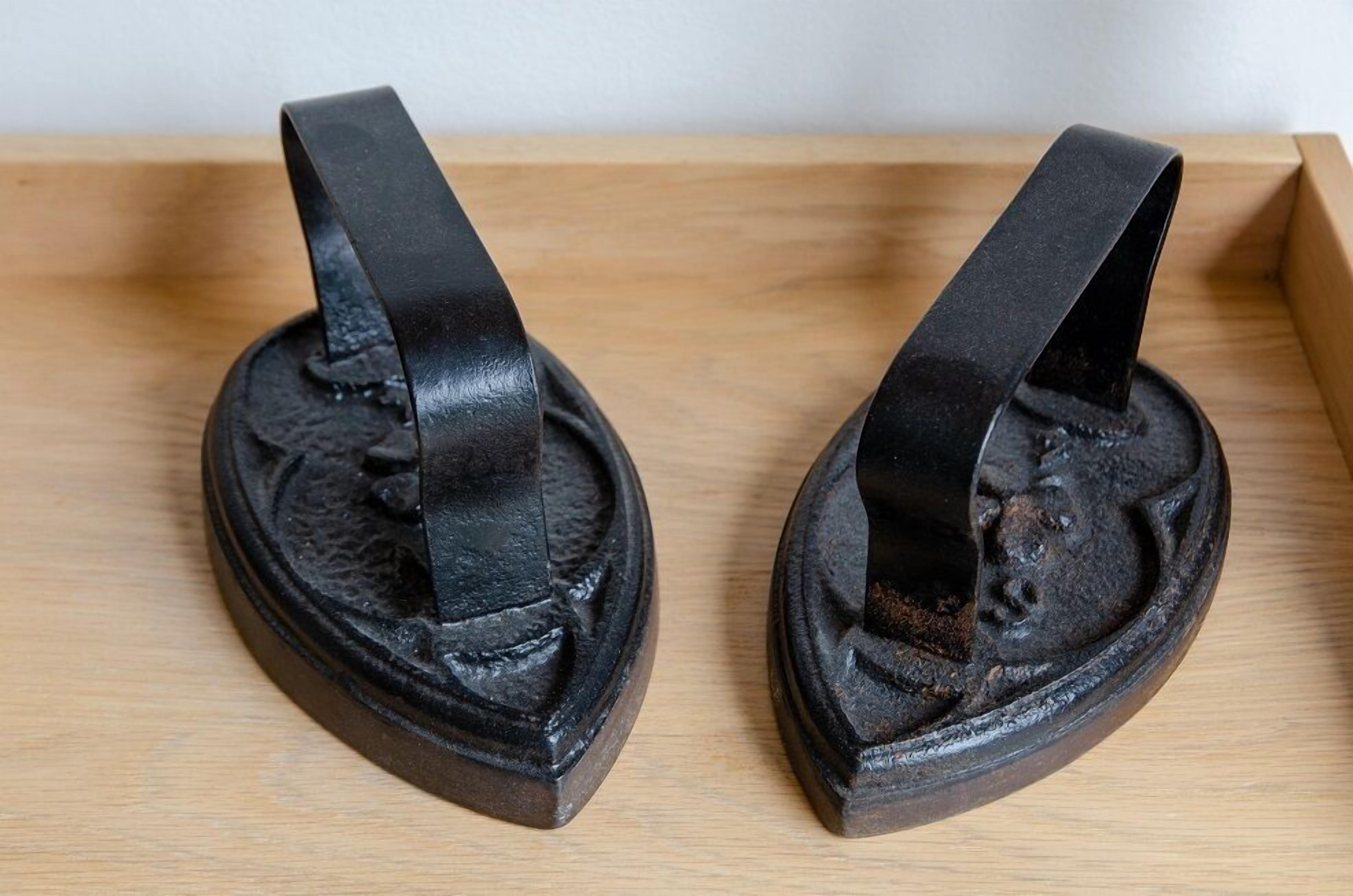 Two black metal shoe horns with a circular base and a handle, placed on a wooden surface.