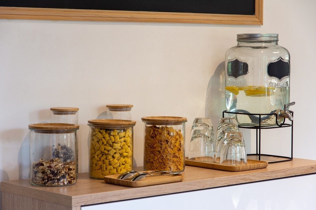 Un comptoir de cuisine sur lequel se trouvent divers bocaux en verre contenant différents aliments, un grand bocal en verre avec un couvercle en métal, et un présentoir en métal avec plusieurs verres.