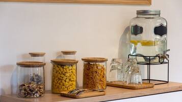 Un comptoir de cuisine sur lequel se trouvent divers bocaux en verre contenant différents aliments, un grand bocal en verre avec un couvercle en métal, et un présentoir en métal avec plusieurs verres.