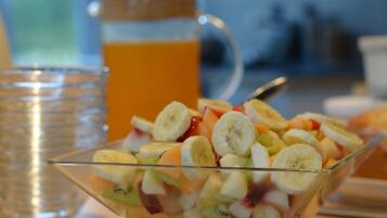 A glass bowl filled with a fruit salad, a glass of orange juice, and a pitcher of orange juice in the background.