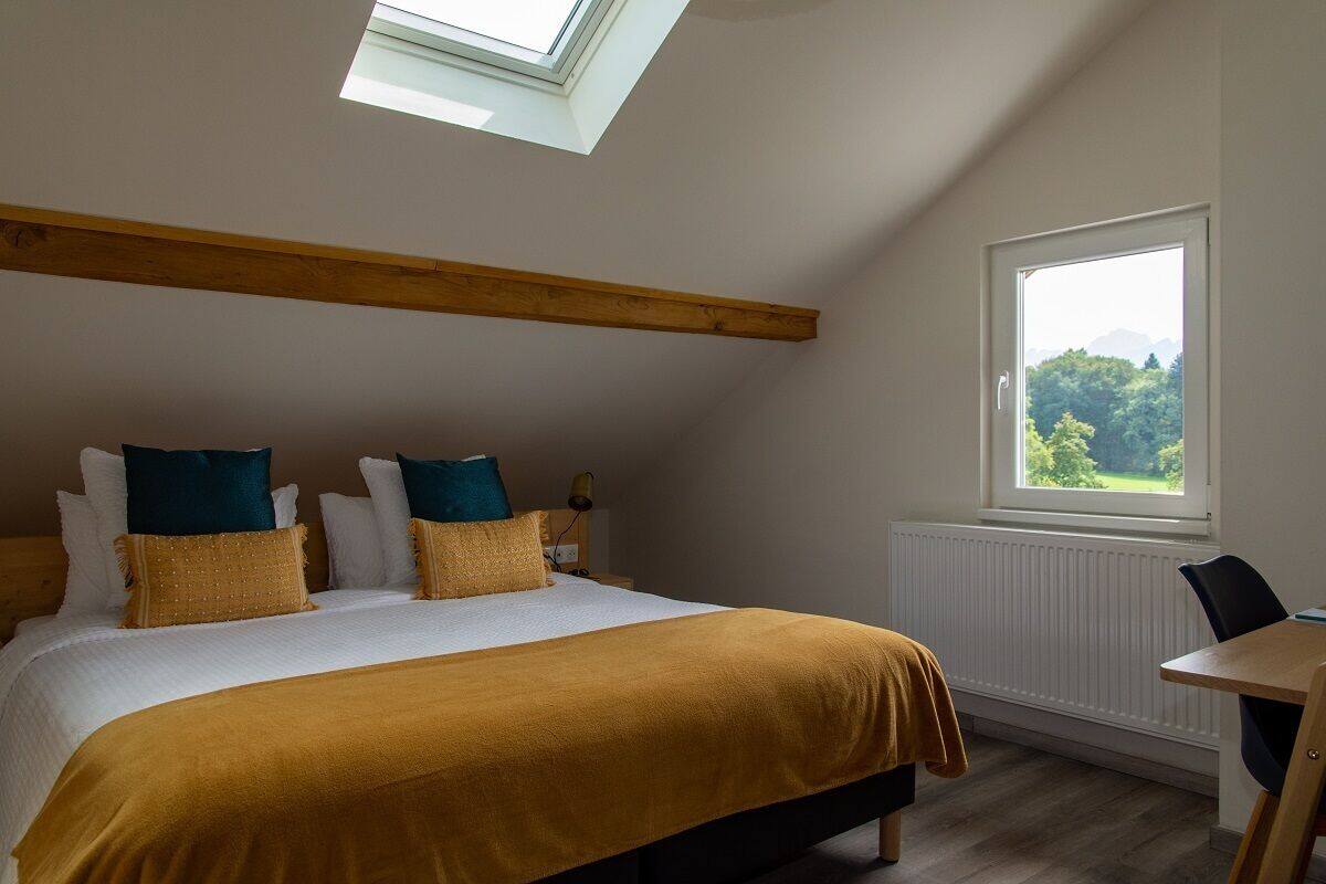 A bedroom with a skylight, a large bed with multiple pillows, a wooden headboard, a window with a view, and a small table.