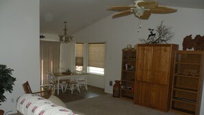 A living room with a beige sofa, a wooden bookshelf, and a dining area with a table and chairs. - The Cozy Cabin LaPine (La Pine)