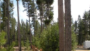 A wooden fence in a forested area with pine trees and a white trailer in the background. - The Cozy Cabin LaPine (La Pine)