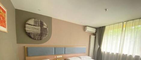 Habitación de hotel con dos camas individuales, un adorno circular en la pared, un equipo de aire acondicionado y una ventana con cortinas.